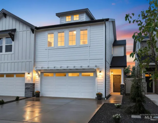Modern multi-story exterior featuring white horizontal siding, a custom pergola over the garage, dark-trimmed window accents, and stone veneer foundation detailing
