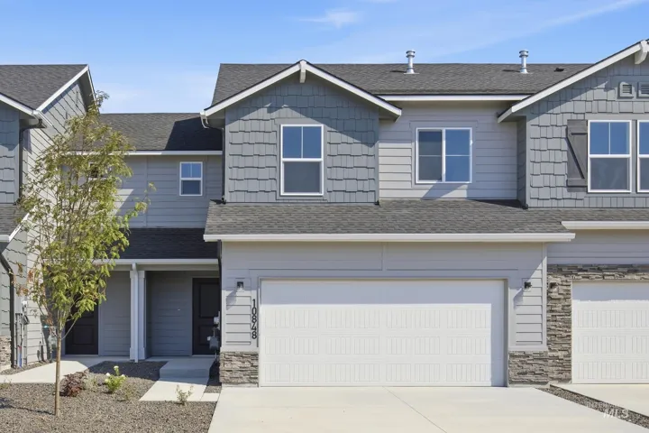Contemporary townhouse exterior featuring a two-car garage, stone veneer accents, gray siding, and a covered entryway
