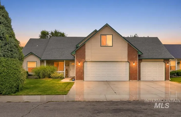 Two-car garage with overhead doors, brick and siding exterior, front porch with columns, and mature landscaping
