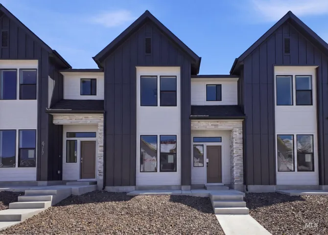 Modern townhome exterior featuring a striking vertical panel siding in a dark tone, contrasting white horizontal siding, stone veneer accents at the entryways, prominent gabled rooflines, and multiple large windows with dark frames