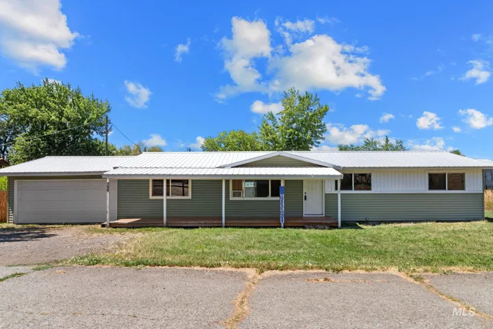 Ranch-style exterior featuring a white metal roof, green and white siding, an attached garage, and a covered front porch with wooden decking