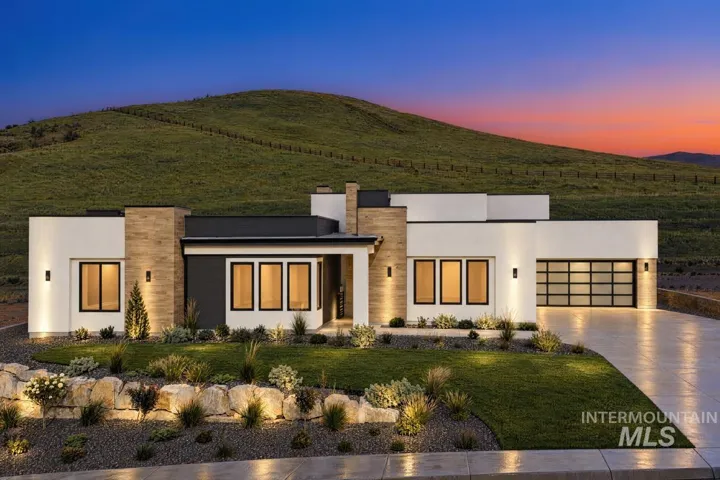 Contemporary single-story exterior featuring smooth stucco siding, stone-finish accents, expansive glass paneled garage door, and tiered rock landscaping