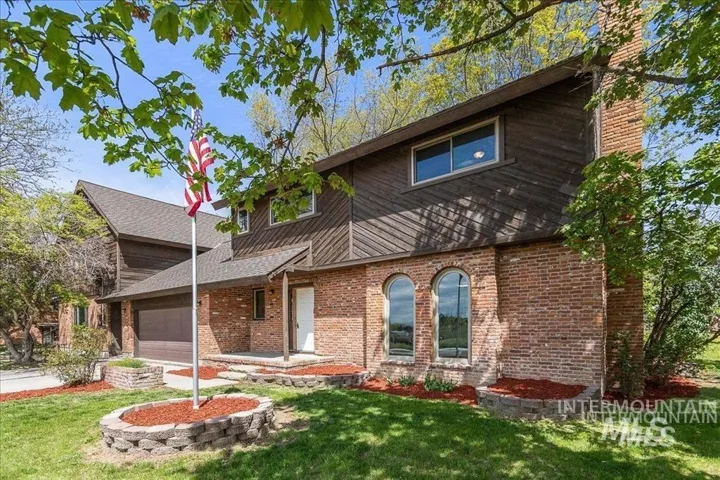 View of front of home with brick siding, a front yard, a garage, a chimney, and a shingled roof