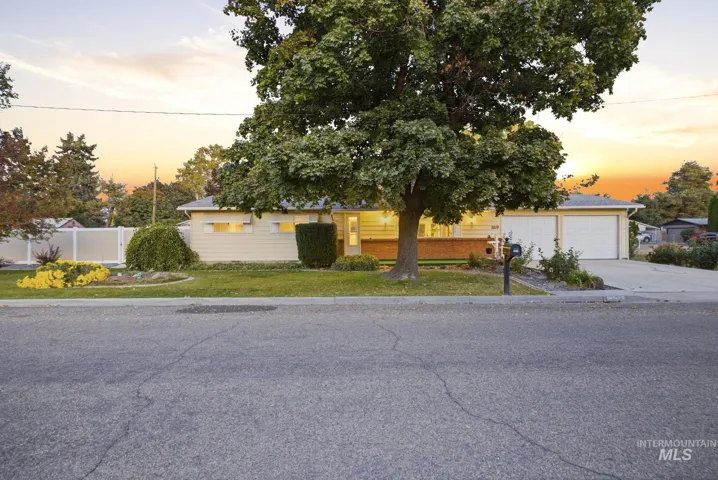 Single-story exterior featuring horizontal siding, brick masonry detailing, an attached two-car garage, and mature landscape elements