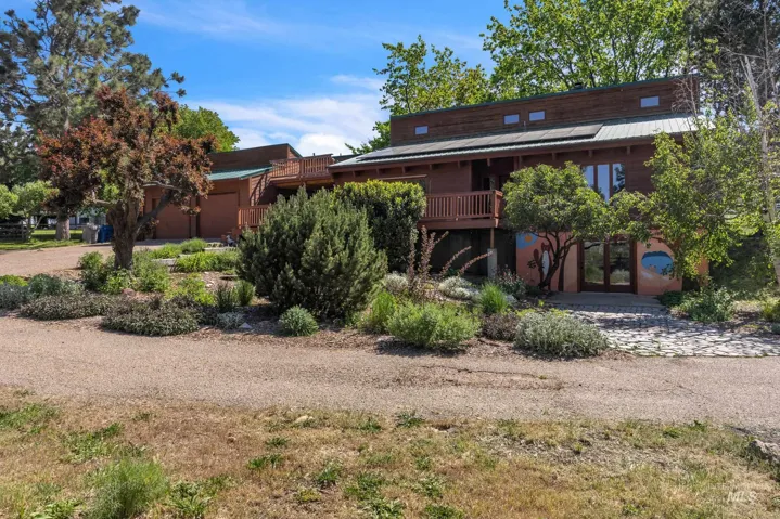 Wood-sided exterior with a metal roof, featuring a raised deck, multi-pane windows, and a landscaped frontage with established plantings