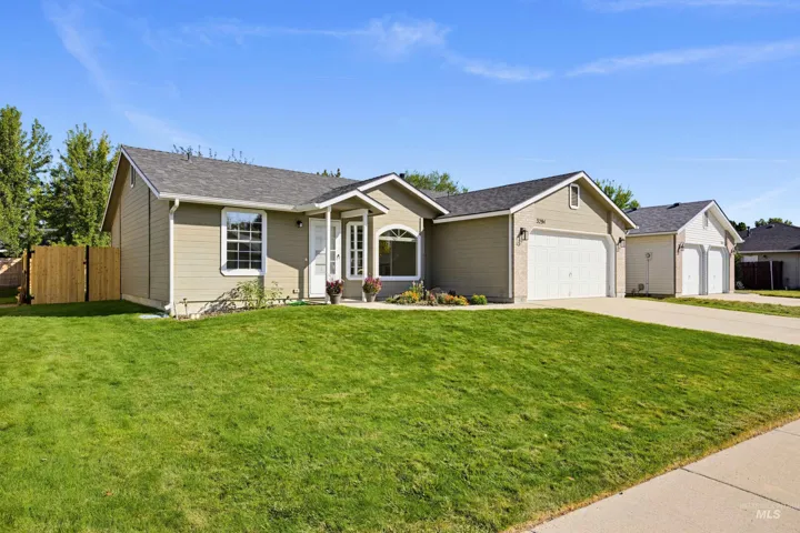 Single-story residence featuring a two-car garage, front yard with green lawn, and a wood privacy fence