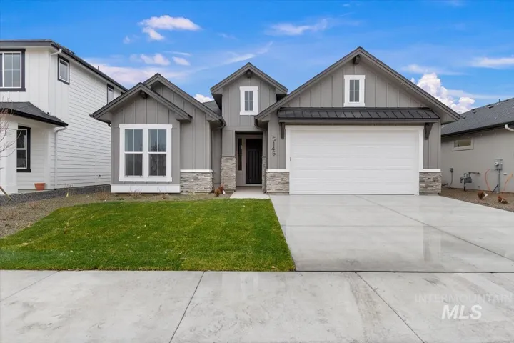 Single-story residence featuring vertical siding, stone masonry accents, a metal-accented roofline, and a paved concrete driveway