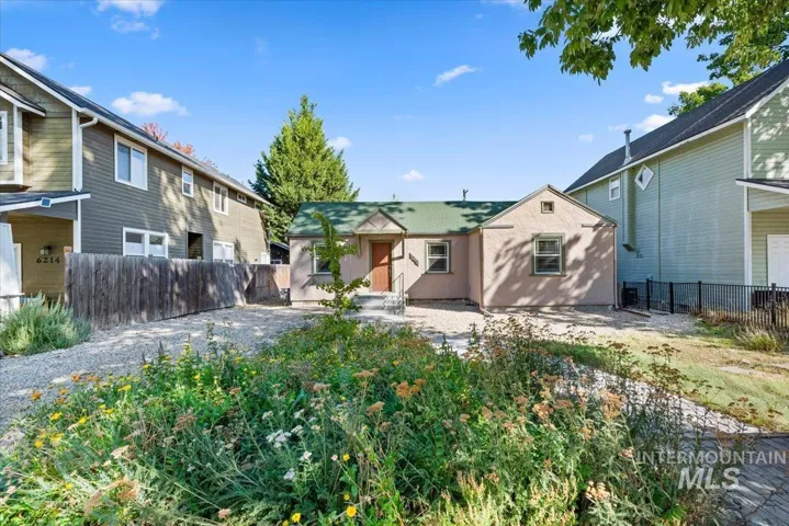 Stucco exterior with a green shingle roof, complemented by a gravel parking area and established perimeter fencing