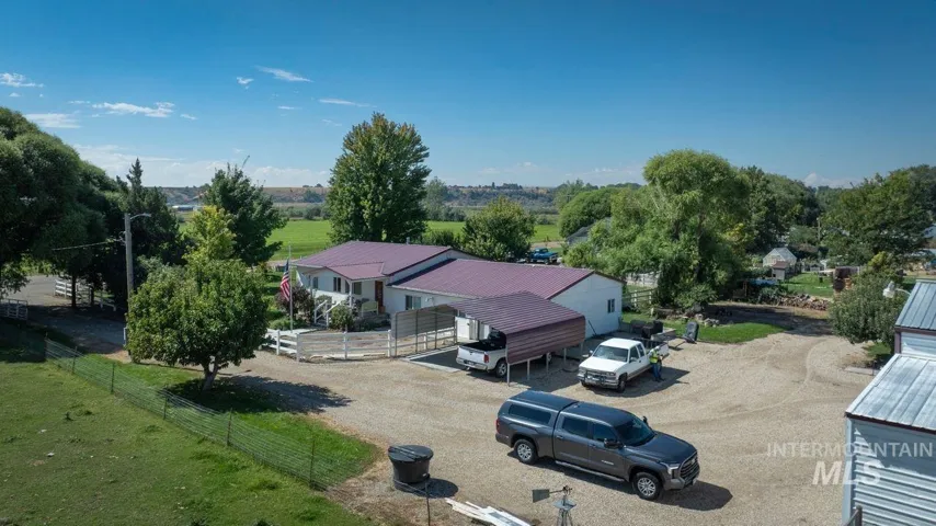 Spacious rural property featuring a modern single-story residence with a metal roof, situated on expansive grounds with mature landscaping, multiple outbuildings, and ample parking and vehicle storage areas