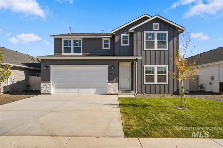 Two-story exterior featuring dark vertical siding, stone veneer accents, an attached two-car garage, and multi-pane windows