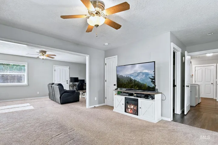 Carpeted flooring, ceiling fan with light fixture, light gray wall color, white interior doors, and wood-finish flooring in an adjacent area