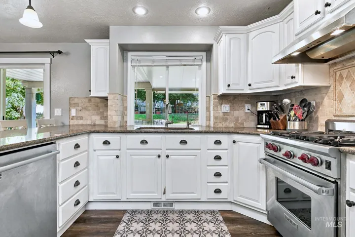 White cabinetry with dark hardware, stone-look countertops, tiled backsplash, stainless steel range, and wood-finish flooring