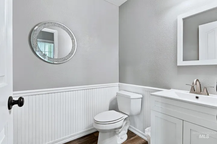 White beadboard wainscoting, wood-finish flooring, and a white vanity with a rectangular sink