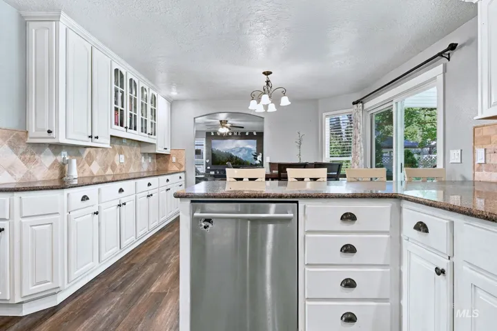 White cabinetry with dark hardware, stainless steel dishwasher, wood-finish flooring, granite countertops, and tile backsplash