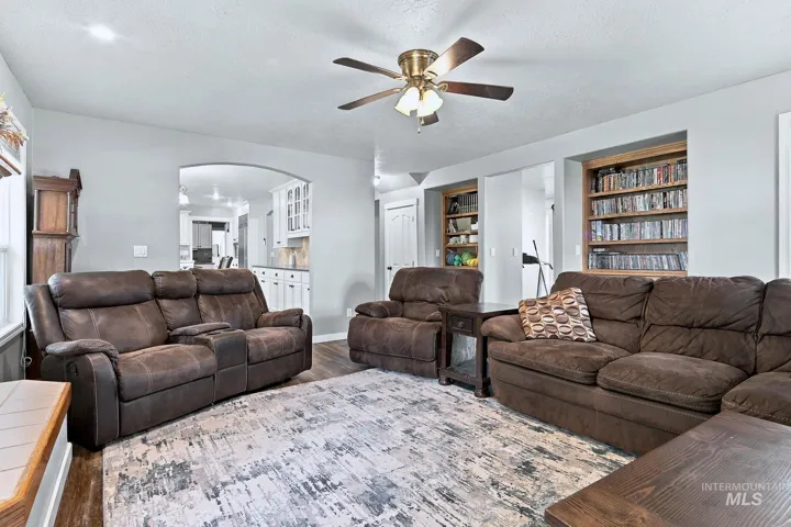 Recessed built-in shelving, wood-finish flooring, ceiling fan with integrated lighting, and an arched doorway