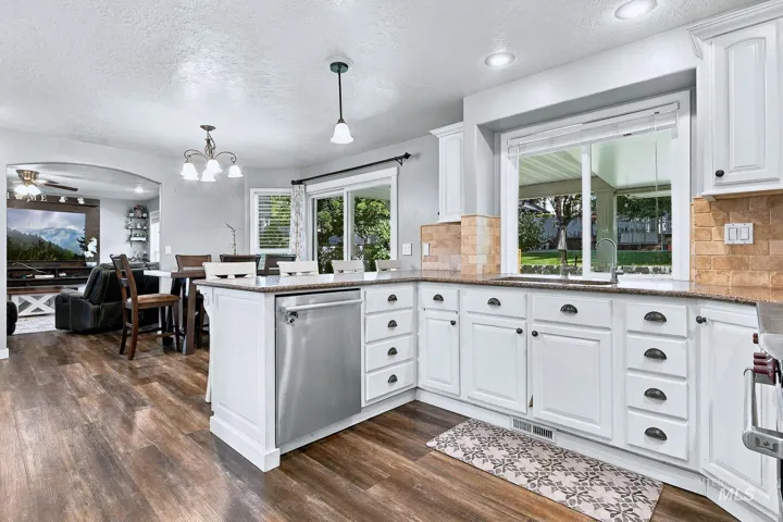 White shaker-style cabinetry with dark hardware, stainless steel dishwasher, brown wood-finish flooring, and a stone-finish countertop