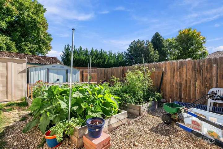 Fenced backyard featuring wood raised garden beds, a gravel ground cover, and two storage sheds