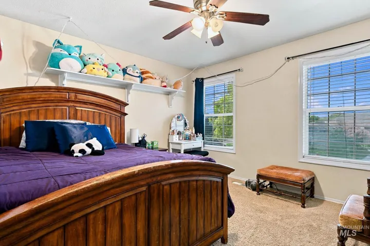 Carpeted room featuring a ceiling fan with integrated lighting, two windows with blinds, and built-in wall shelving