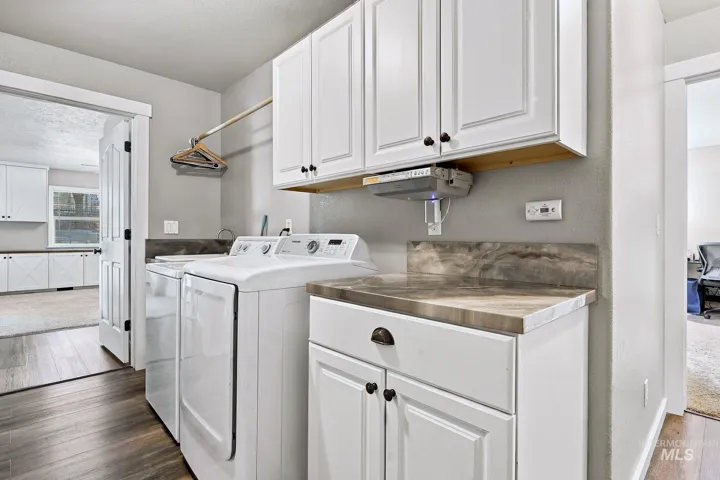 Laundry area featuring wood-finish flooring, white cabinetry, integrated countertop, and a clothes hanging rod