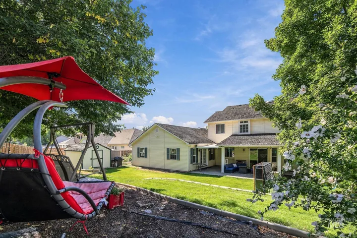 Expansive backyard featuring a manicured lawn, established landscaping, and a covered patio area