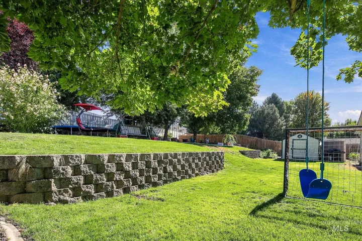 Expansive backyard featuring a tiered lawn with a stone retaining wall, mature trees, and a storage shed
