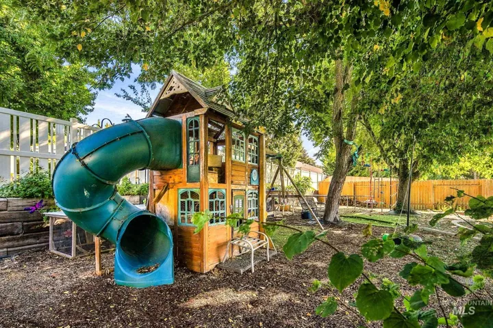 Expansive yard featuring a wood play structure with an attached slide, mature trees, and a privacy fence