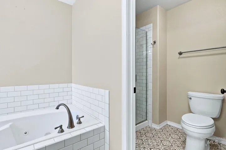 Soaking tub with subway tile surround, tiled shower with glass enclosure, toilet, and patterned floor tile