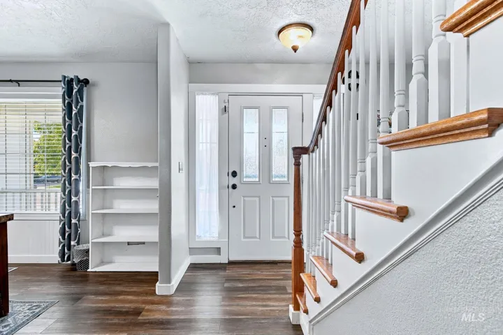 Entryway featuring wood-finish flooring, a white paneled door with decorative glass, and a traditional staircase with turned balusters and wood handrails