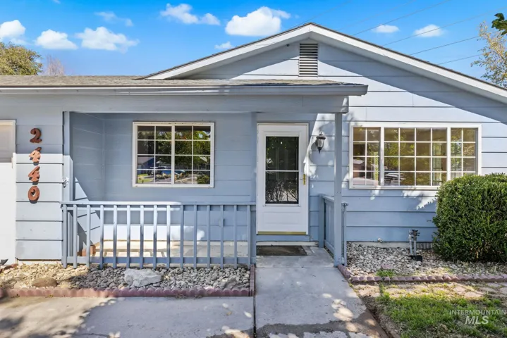 Exterior featuring light blue siding, a covered porch with railing, a paneled entry door, and multi-pane windows