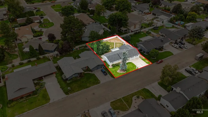 Aerial perspective of a property featuring a multi-car attached garage, a concrete driveway, a paved walkway, mature trees, and a fenced backyard