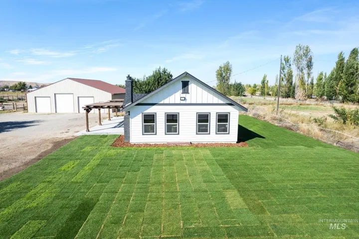 White exterior with dark trim windows, covered patio, large detached garage, and a newly sodded lawn