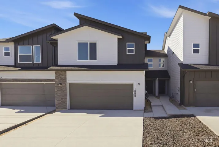 Contemporary multi-level townhome featuring a dual-tone facade, prominent gray garage doors, a concrete driveway, and a stone accent column