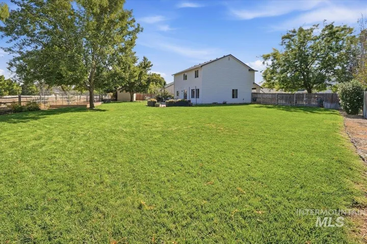 Expansive backyard featuring a manicured lawn, mature trees, and perimeter fencing