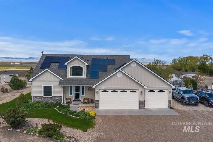 Contemporary residence featuring a light-toned siding exterior with stone accents, a multi-car garage, a prominent dormer window, and integrated solar panels