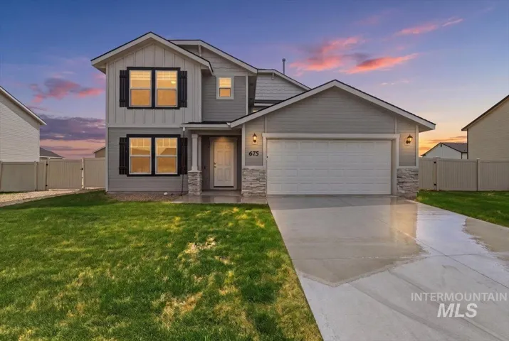 Two-story residence featuring light gray siding with board and batten accents, a two-car garage, stone veneer pillars, and a privacy fence