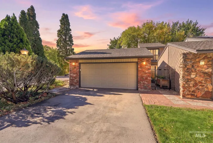 Attached two-car garage with a panel door, brick facade, and exterior lighting