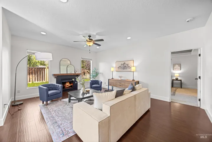 Spacious living area featuring rich wood-finish flooring, a contemporary fireplace with a dark mantel, abundant natural light from multiple windows, recessed lighting, and a ceiling fan