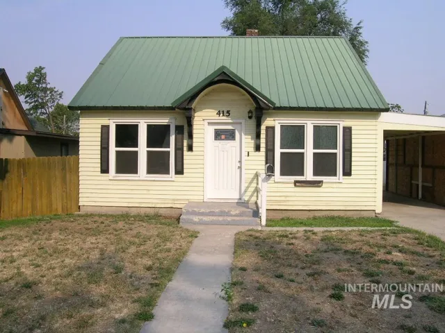 Exterior featuring light-colored horizontal siding, a green metal roof, decorative front door gable with arched brackets, shuttered windows, and a side carport