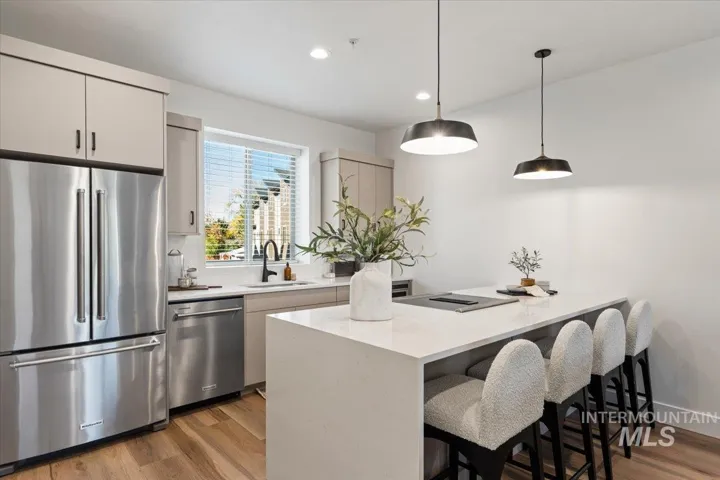 Kitchen featuring a waterfall-edge island with solid-surface countertops, stainless steel appliances, matte black plumbing fixtures, wood-finish flooring, and pendant lighting