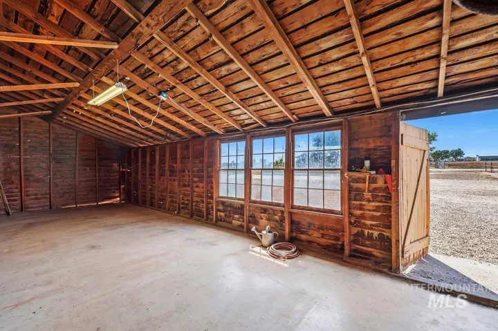 Spacious garage interior featuring an exposed wood beam ceiling, multiple window panes, concrete flooring, and a large barn door entry