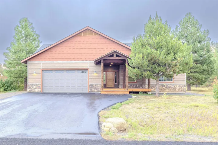 View of front of house featuring stone siding, driveway, a front lawn, and a wooden deck