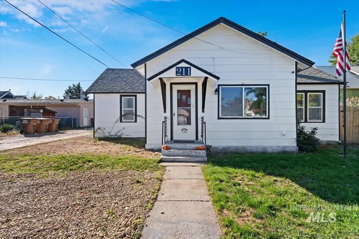 White exterior siding with dark trim, covered front entry, concrete pathway, and an additional structure in the rear