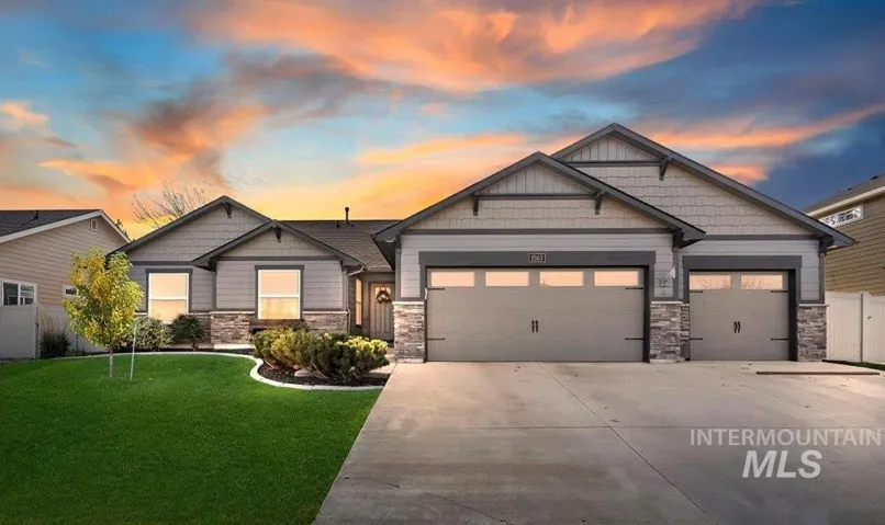 Single-story residence featuring a stone and siding facade, three-car garage, and manicured front lawn with ornamental landscaping