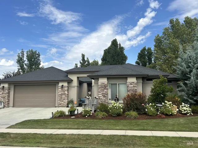 Stucco exterior with stone accents, attached two-car garage, mature landscaping, and a covered entryway
