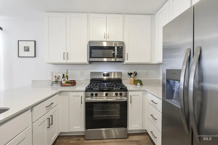 Kitchen featuring white shaker-style cabinetry, solid-surface countertops, stainless steel appliances, and wood-finish flooring