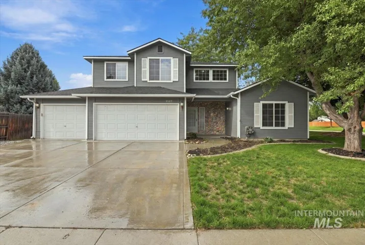 Two-story residence featuring gray siding, a stone facade accent, white window shutters, a two-car garage, and a concrete driveway