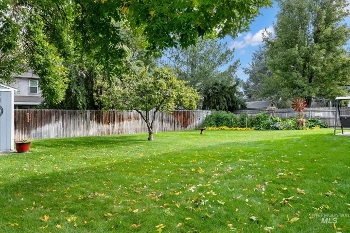 Expansive backyard featuring a level lawn, perimeter wood fencing, mature trees, and planted flower beds