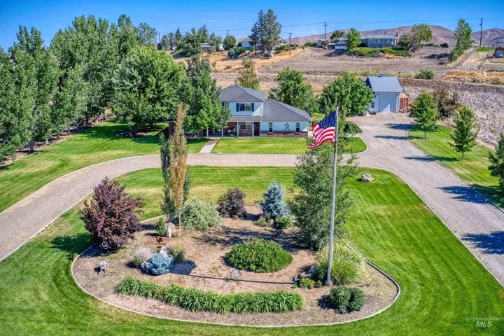 Expansive property featuring a circular gravel driveway, lush green lawn, mature trees, and a detached auxiliary building