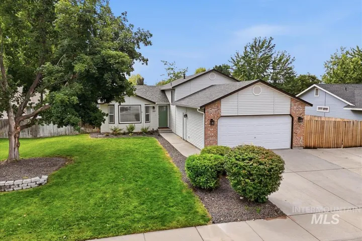 Exterior featuring a two-car garage, brick facade accents, a concrete driveway, established landscaping, and a mature tree