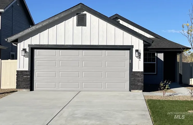 View of front of property with board and batten siding, stone siding, a garage, and concrete driveway